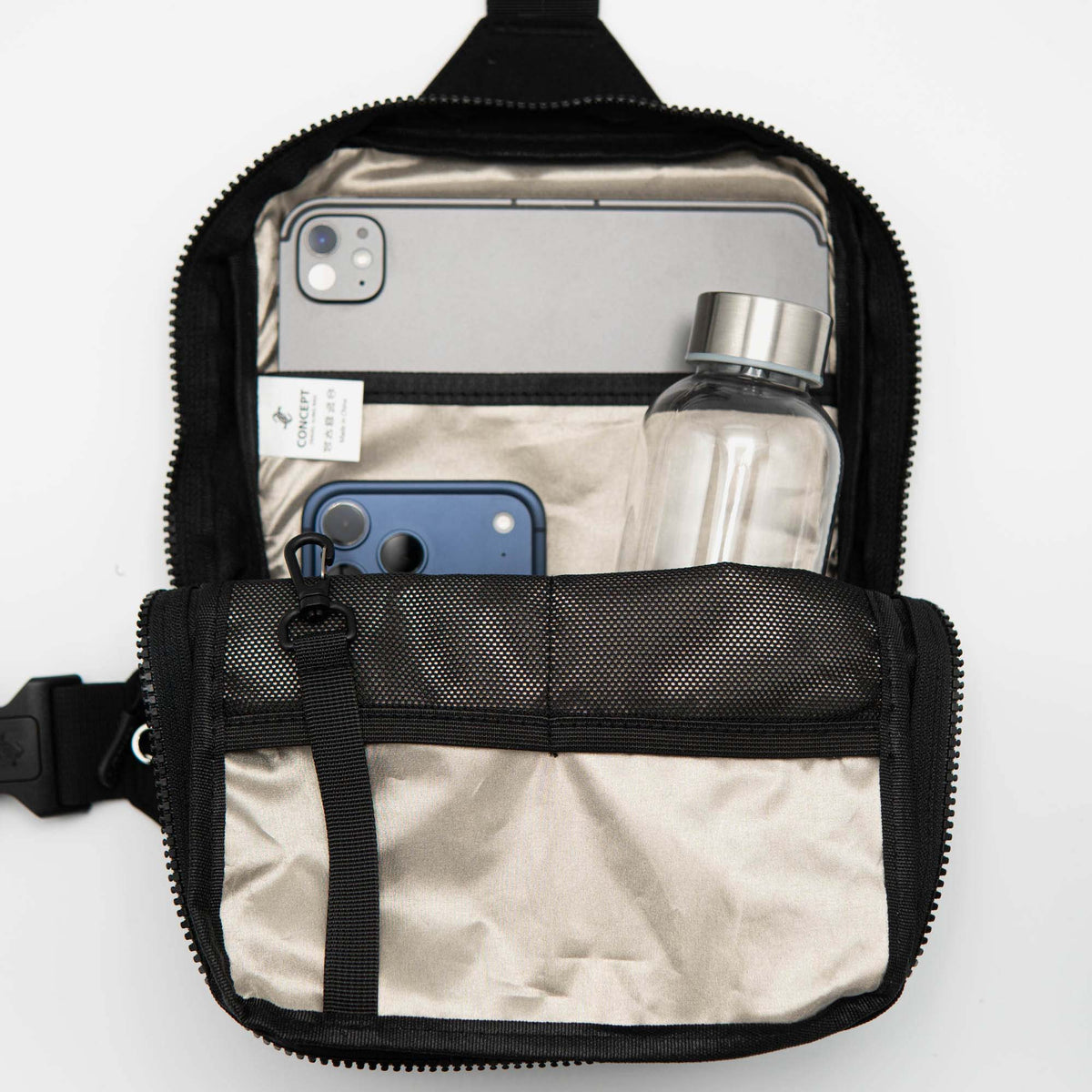 Black crossbody bag with phone, water bottle, and other items on a white background